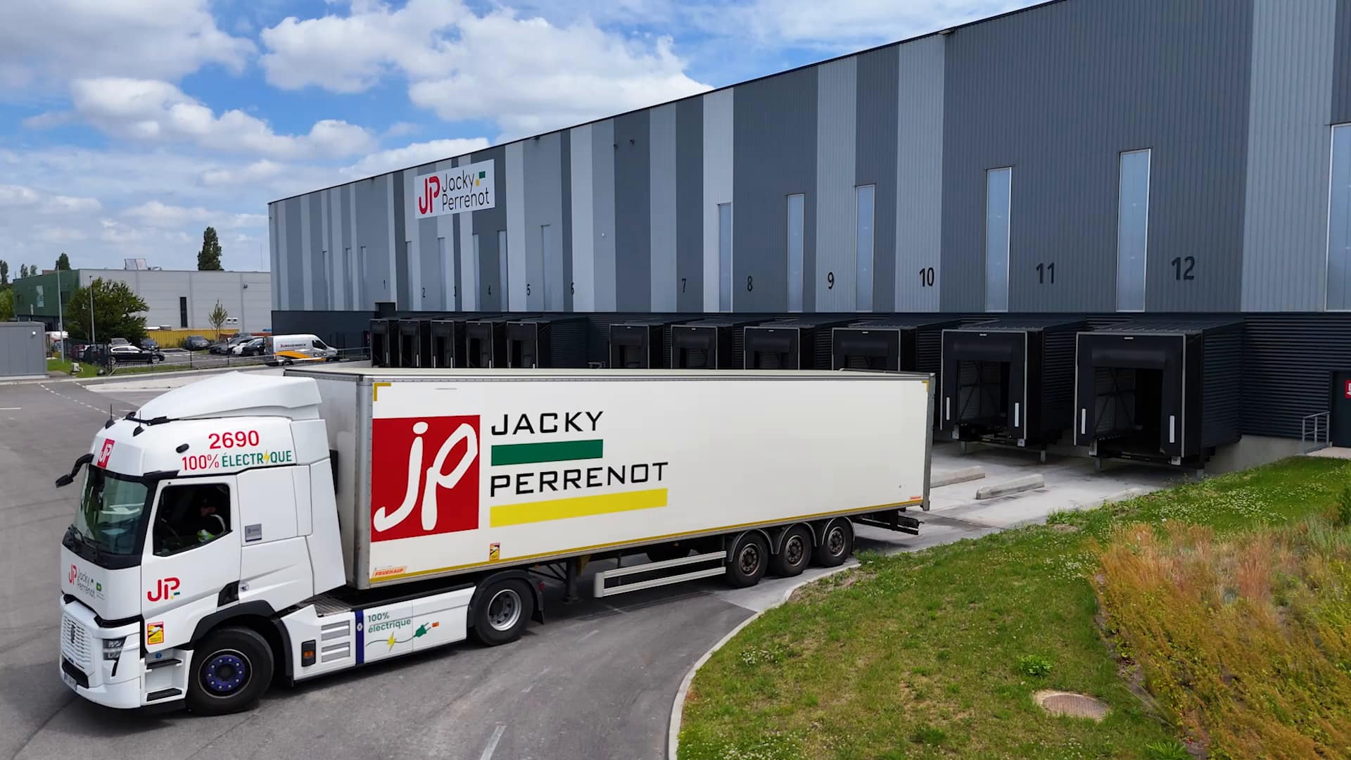 Camion électrique Jacky Perrenot devant les quais de chargement d'un entrepôt logistique