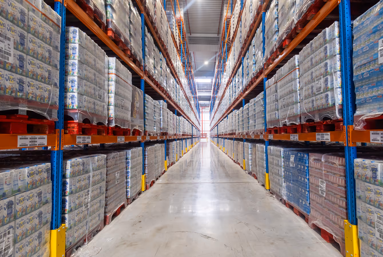 Allée centrale d'un entrepôt Perrenot Logistique, palettes filmées sur racks bleus et orange