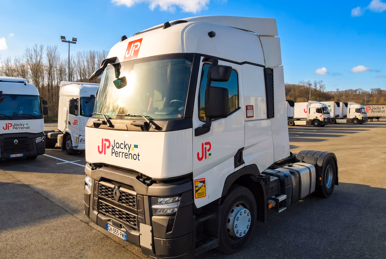 Tracteur routier Jacky Perrenot, cabine blanche au logo, sur le parking du site