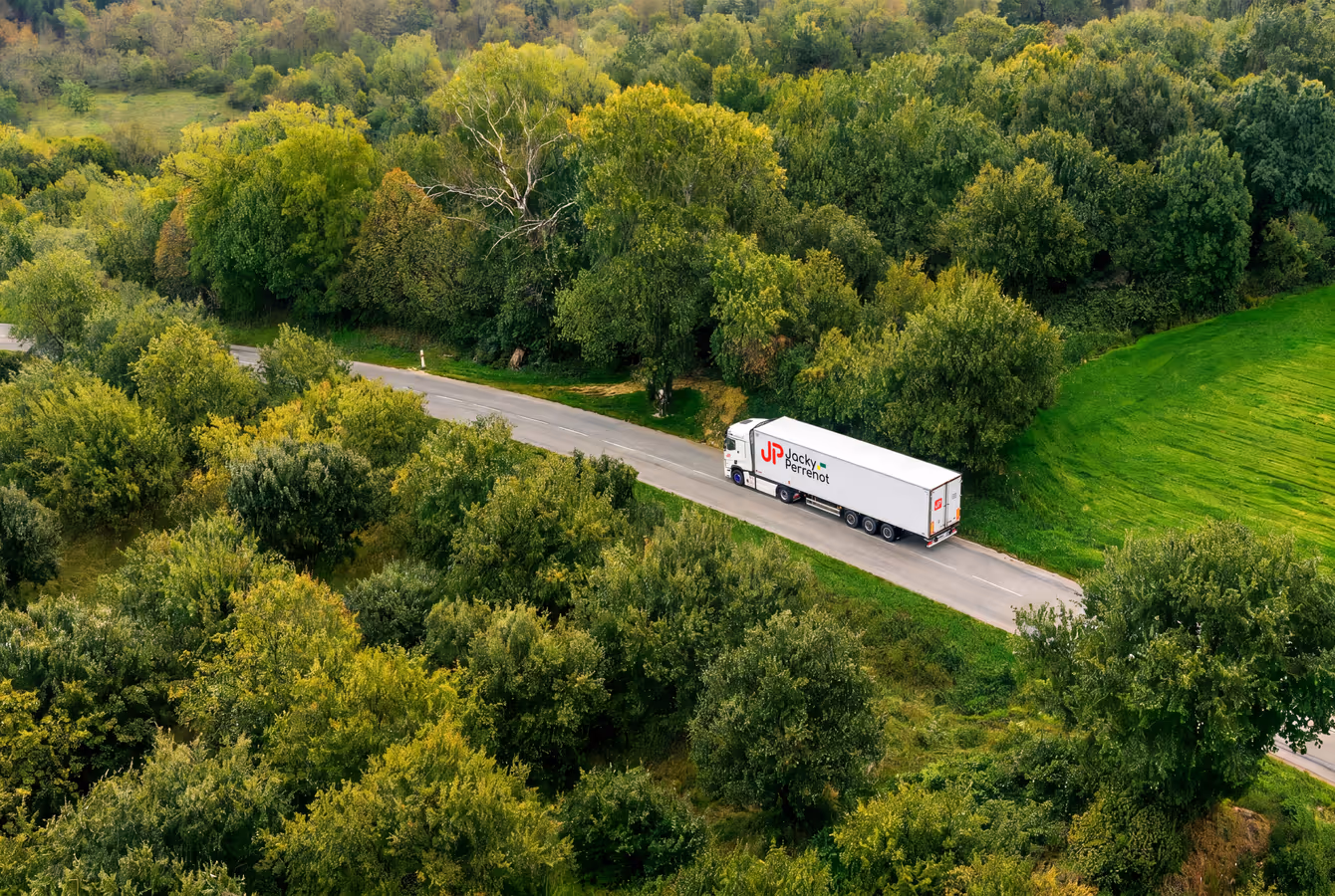 Vue aérienne d'un camion Jacky Perrenot sur une route bordée de forêt